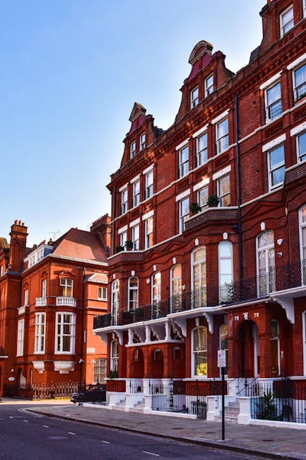 The image shows a row of elegant, white Victorian-style terraced houses with detailed architectural features and large windows, situated along a residential street in Maida Vale. In the foreground, th
